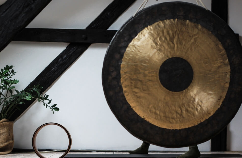 A golden gong and plant against a white wall with wood beams